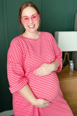 woman wearing a pink and white striped maternity dress and holding her baby bump while smiling