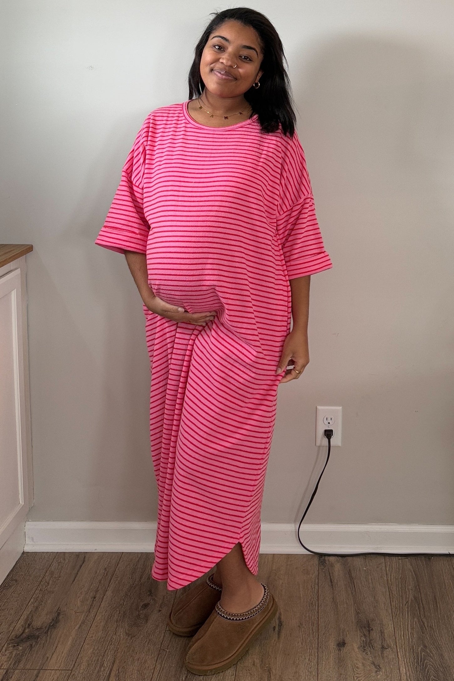 woman wearing a pink and white striped maternity maxi dress and holding her baby bump