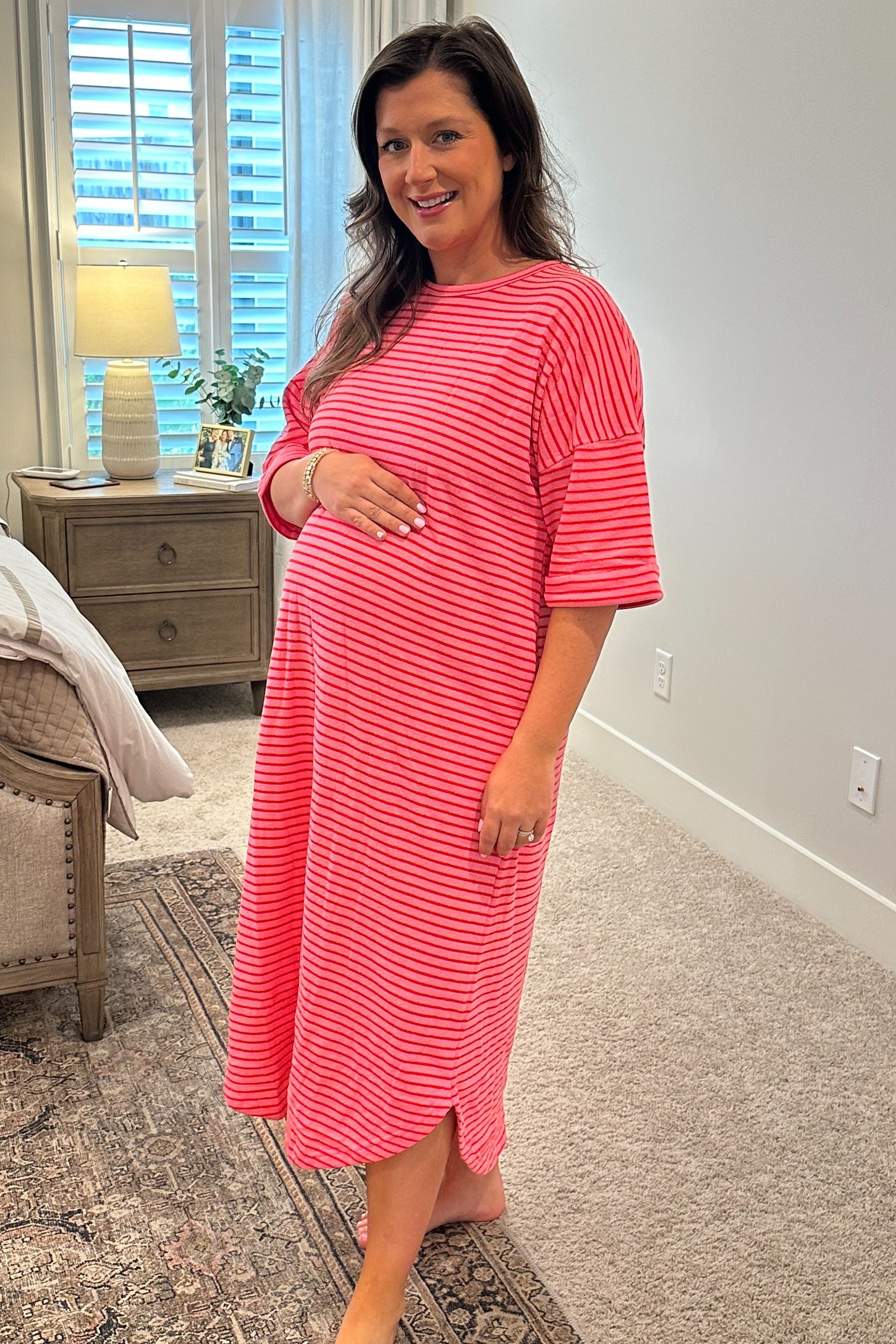woman wearing a coral and white striped maternity dress, gently cradling her baby bump