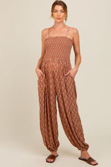 woman wearing a rust patterned maternity jumpsuit with adjustable straps and pockets, showing a baby bump