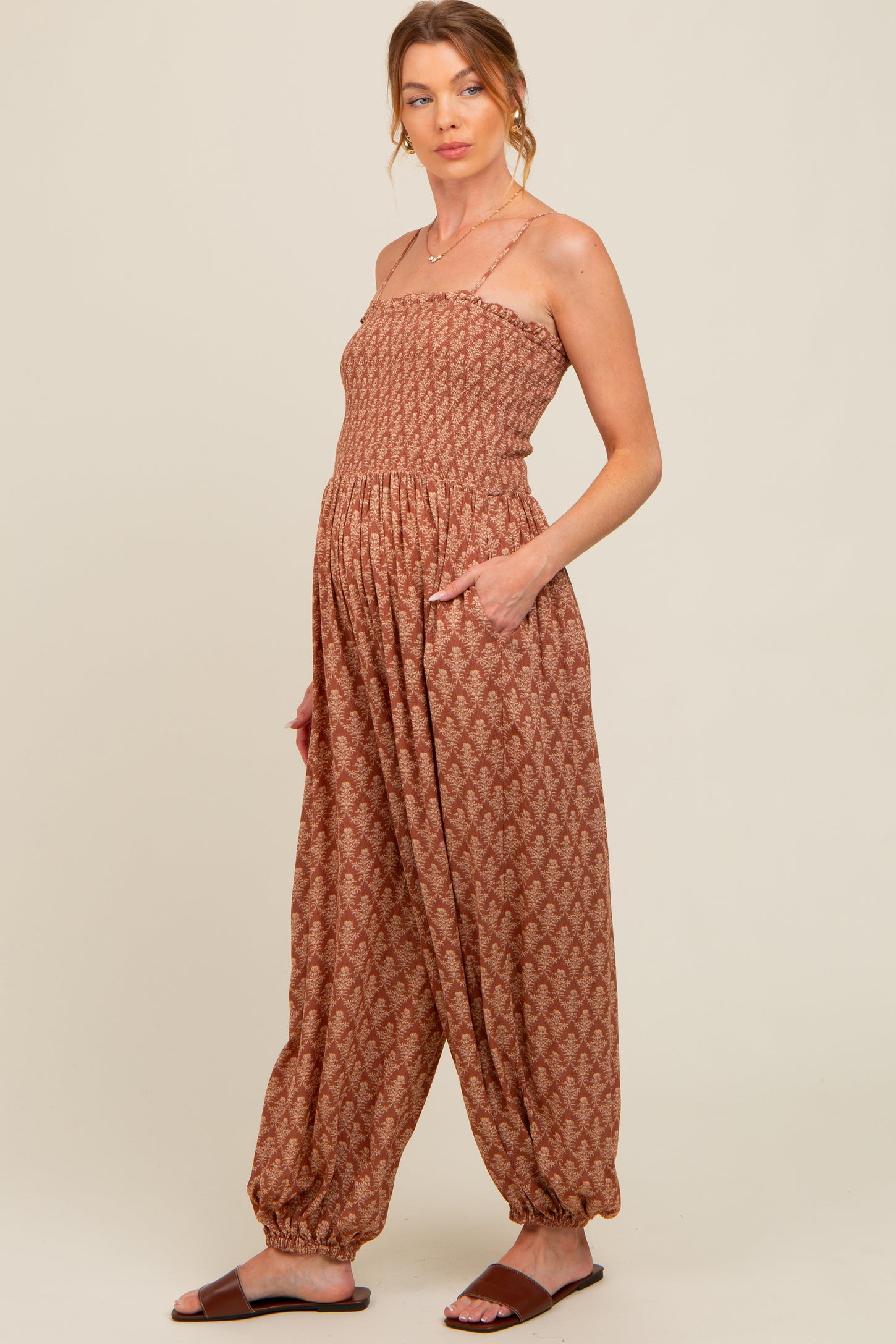 woman wearing a rust-colored maternity jumpsuit with a smocked bodice and wide-leg pants, featuring pockets