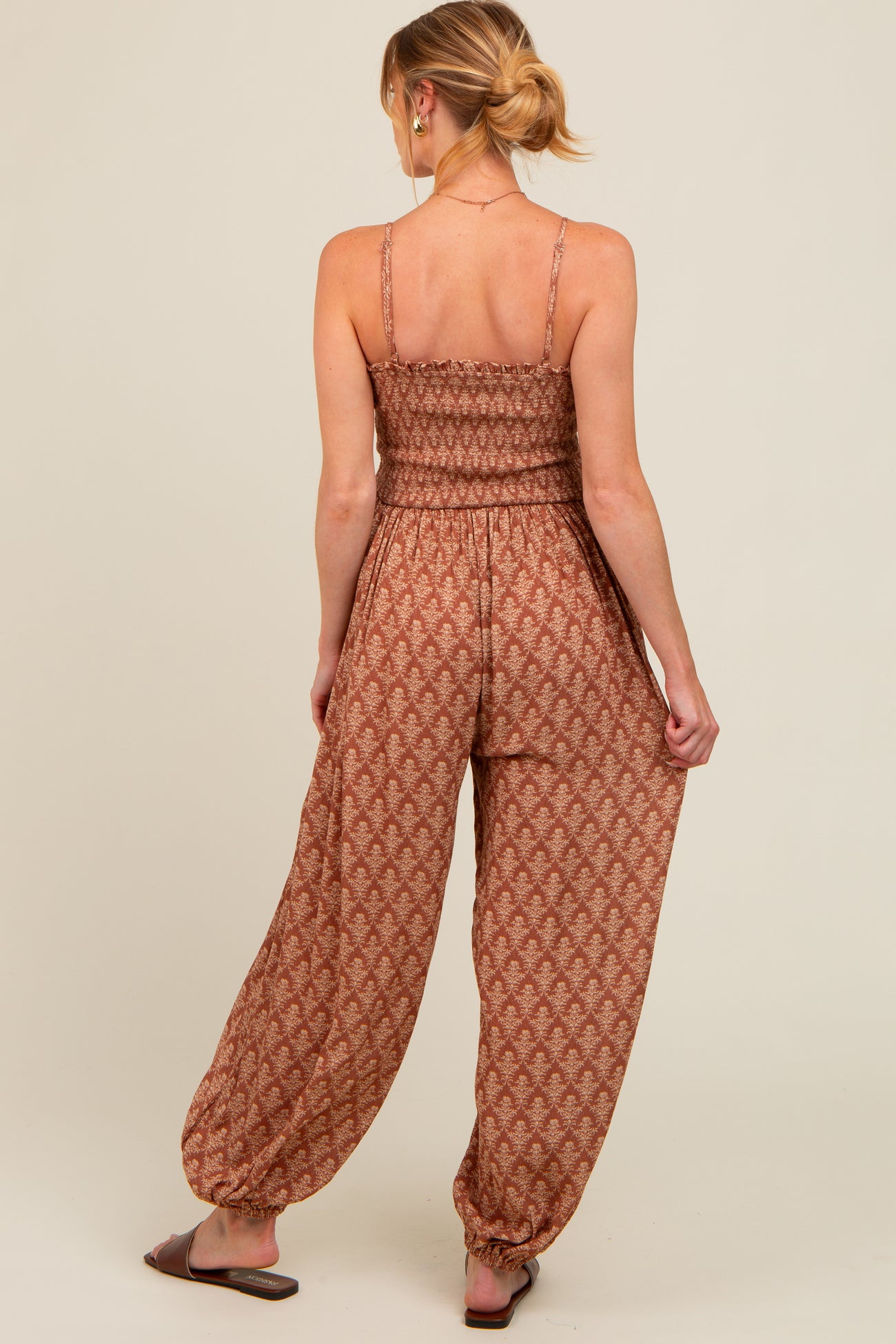 woman wearing a brown patterned maternity jumpsuit with a smocked bodice and relaxed fit pants from the back
