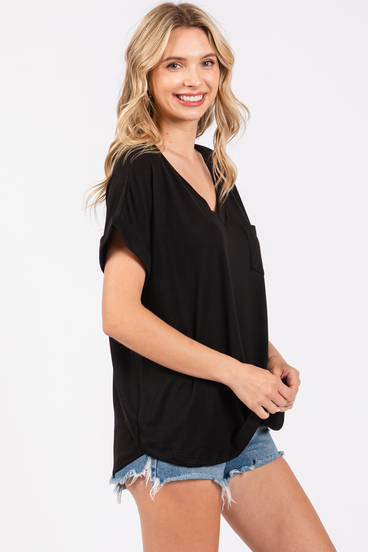 woman wearing a black short sleeve v-neck top with a front pocket and denim shorts