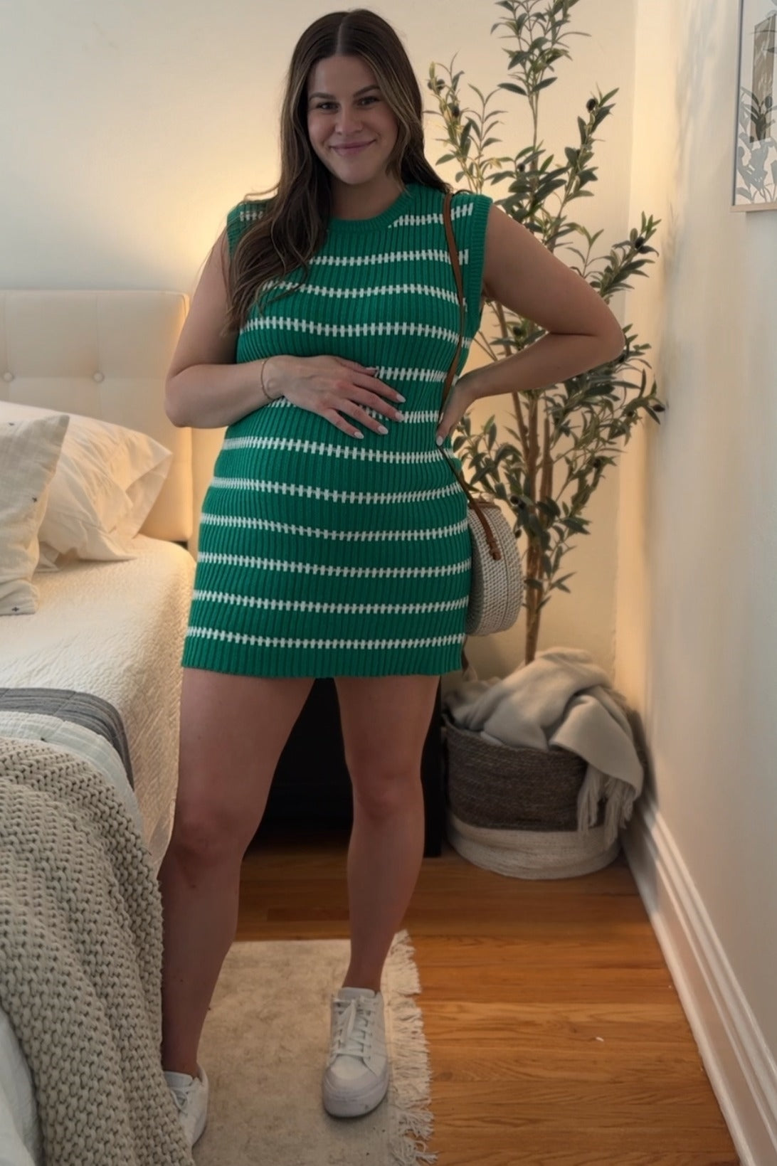 woman wearing a green and white striped sleeveless maternity dress and holding her baby bump
