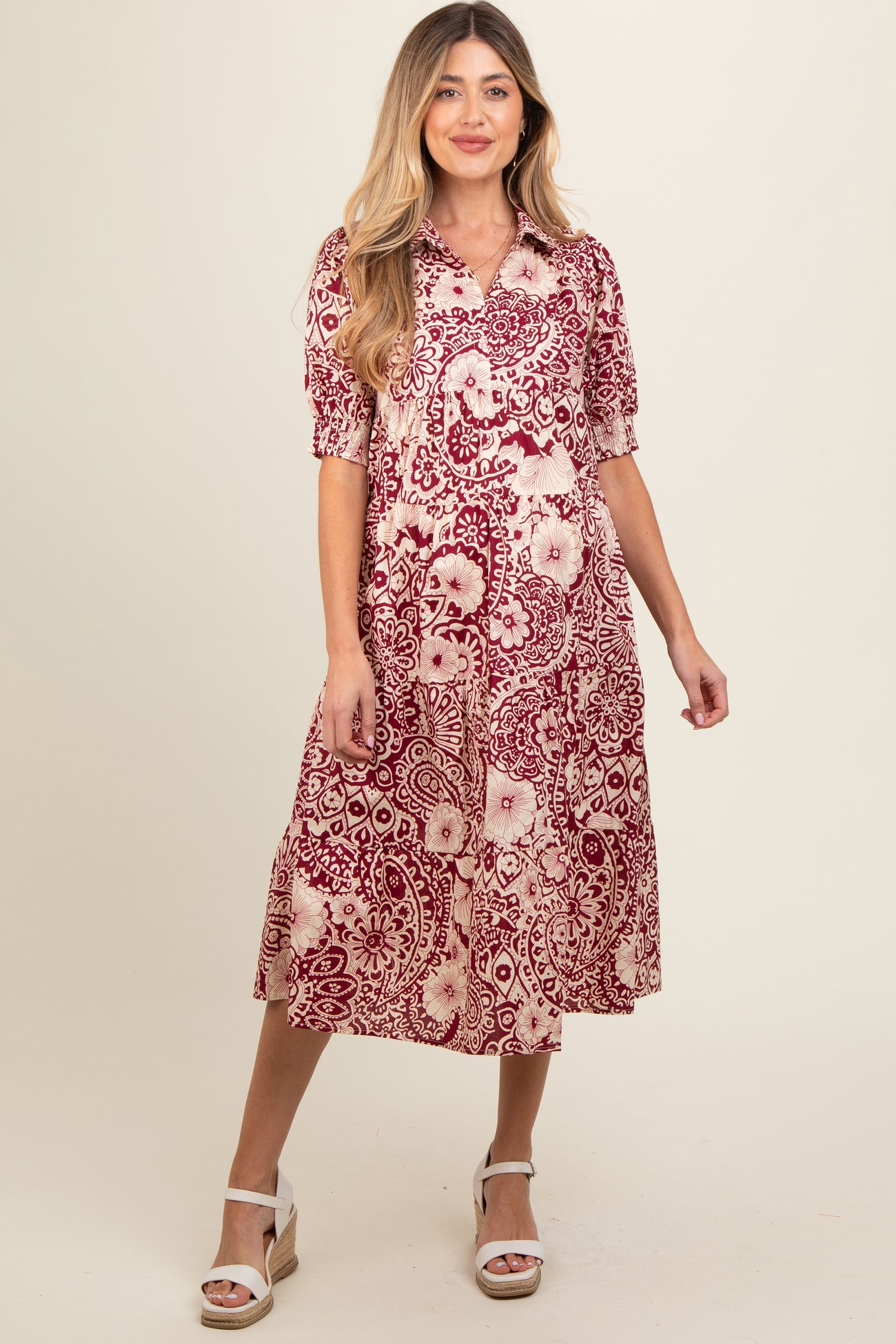 woman wearing a red and cream floral maternity dress with short sleeves and a flowy skirt, showcasing her baby bump