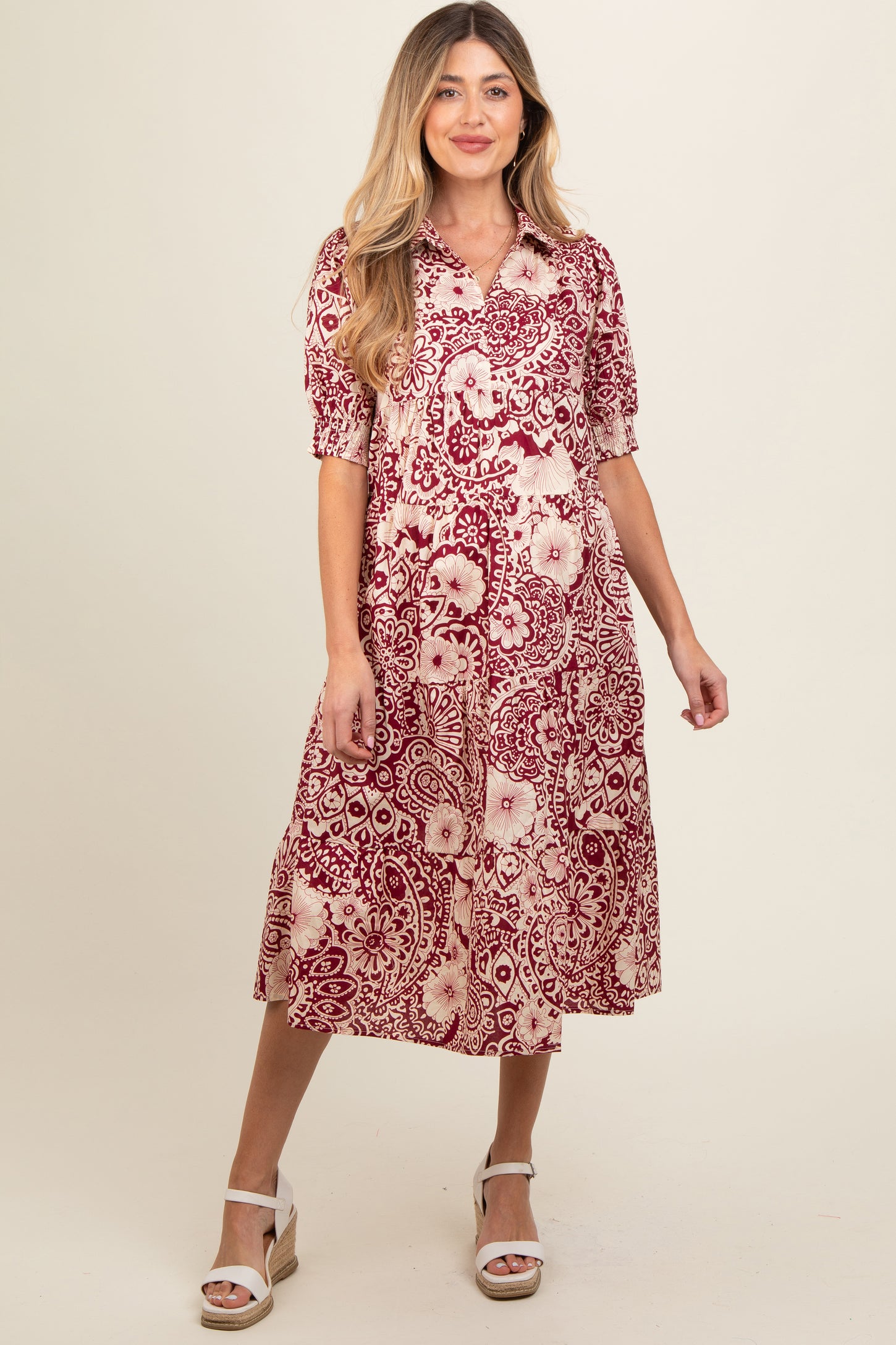 woman wearing a red and cream floral maternity dress with short sleeves and a flowy skirt, showcasing her baby bump