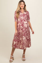 woman wearing a red and cream floral maternity dress with short sleeves and a flowy skirt, showcasing her baby bump