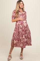 woman wearing a maroon floral print maternity dress with a collared neckline and short sleeves, holding her baby bump