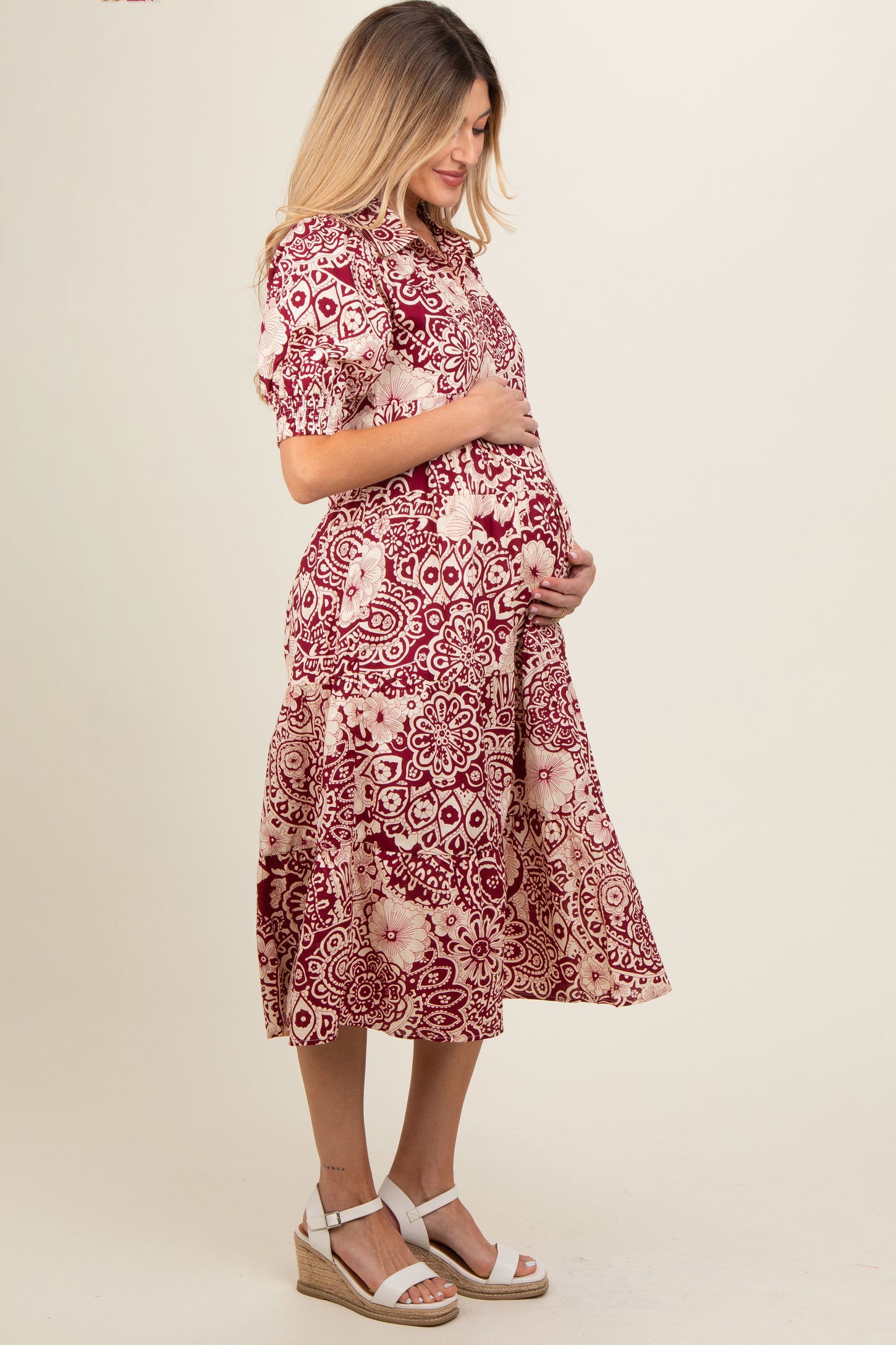 woman wearing a burgundy floral print maternity dress and holding her baby bump