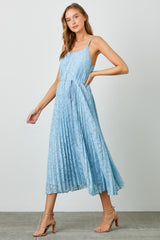 woman wearing a light blue sleeveless pleated maxi dress with a cinched waist and strappy heels