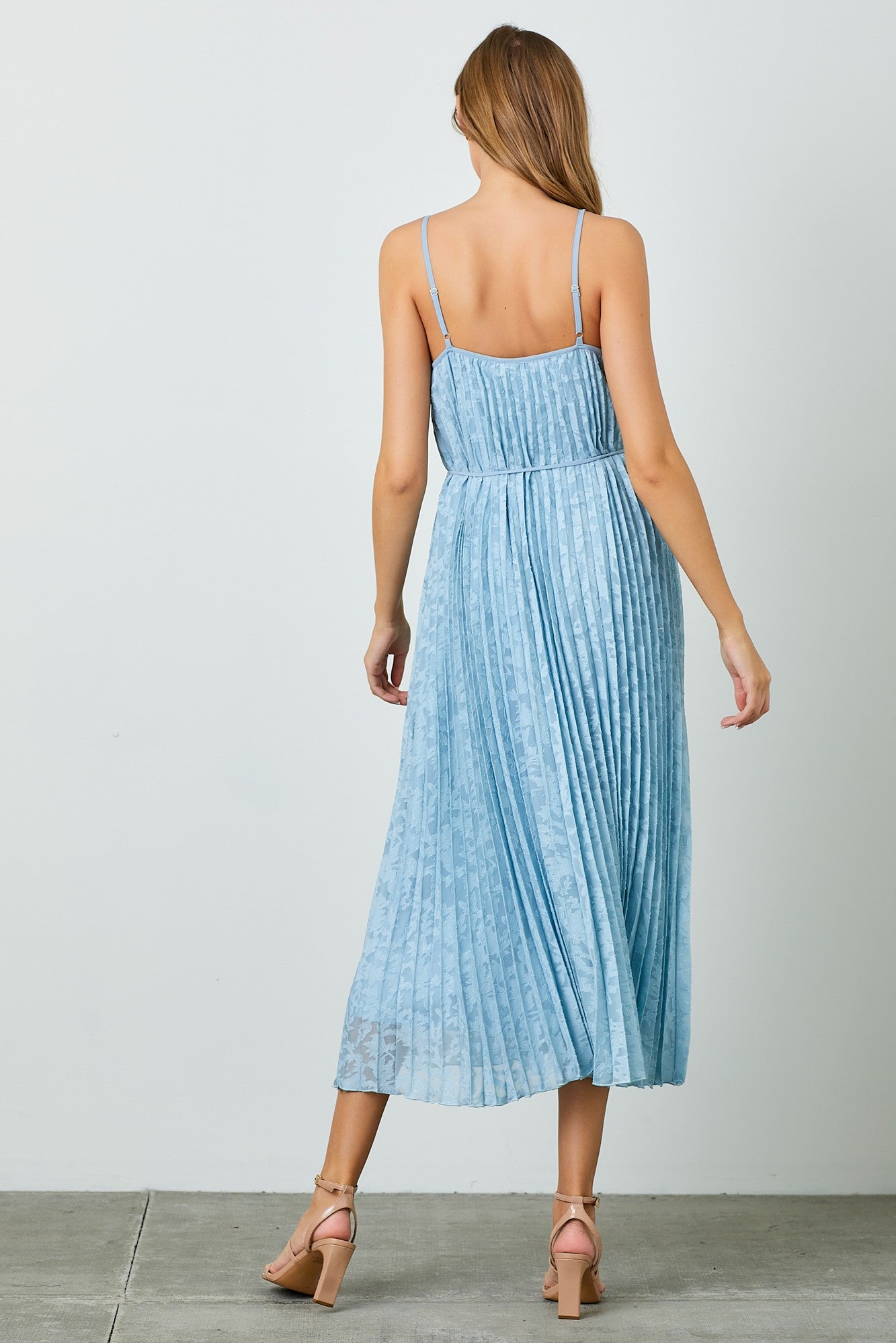 woman wearing a light blue pleated maxi dress with adjustable straps and a cinched waist, viewed from the back