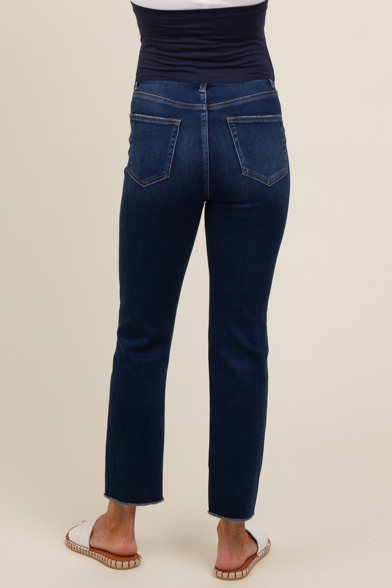 woman wearing dark blue maternity jeans, showing back view with a slim fit and frayed hem.