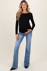woman wearing a black long sleeve maternity top and blue flared jeans, gently holding her baby bump