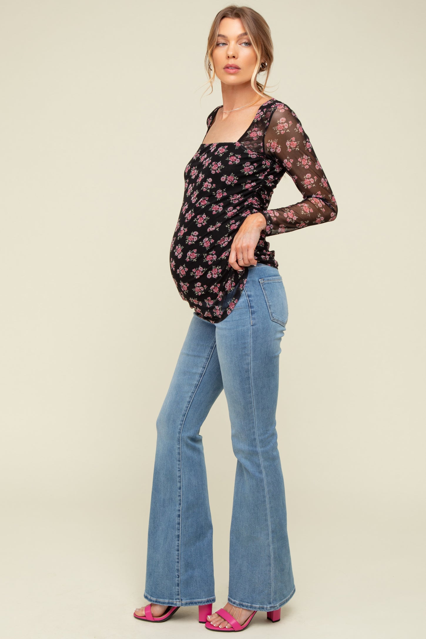 woman wearing a black floral maternity top with long sleeves and blue flared jeans, showing her baby bump