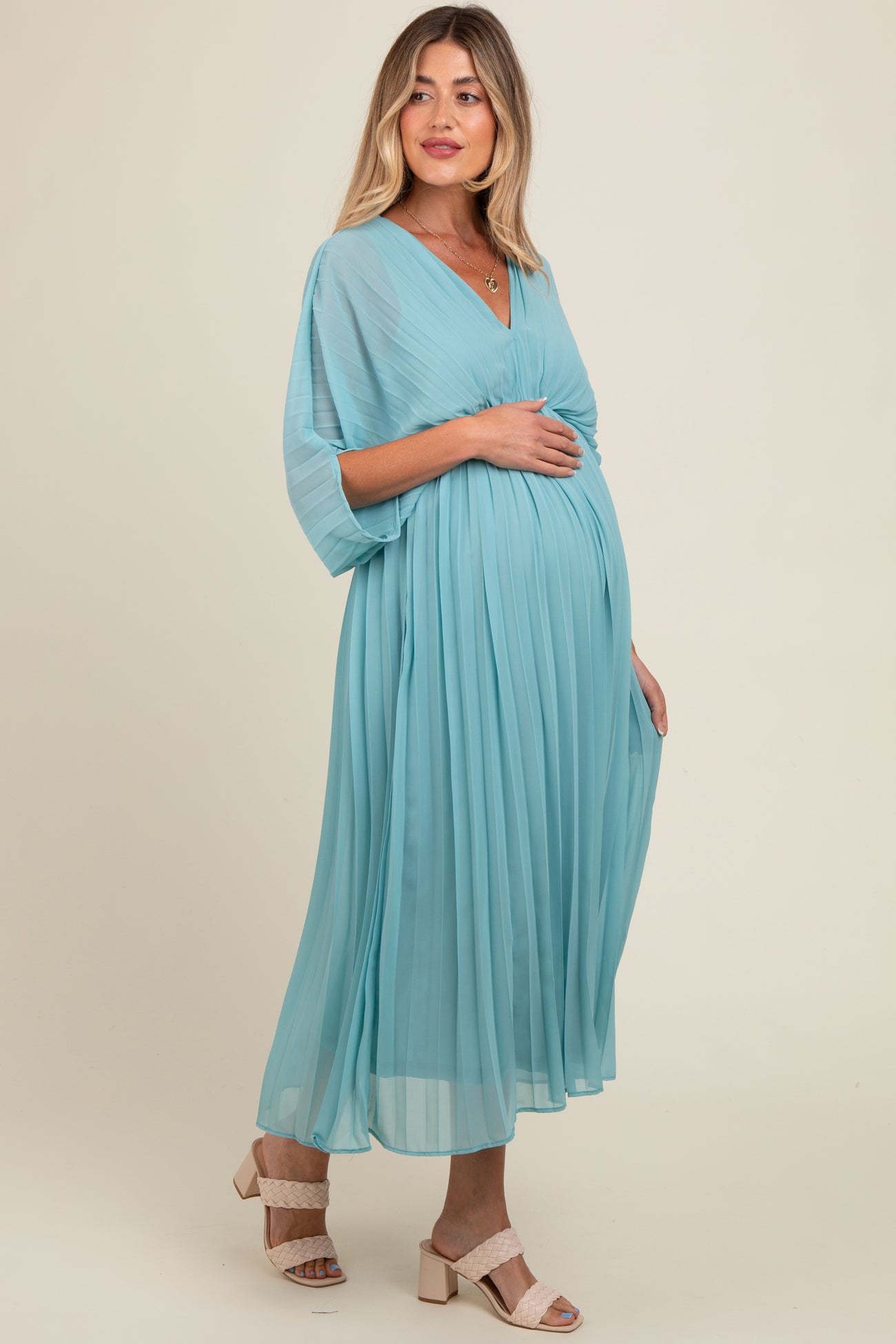 woman wearing a light blue pleated maternity dress with a v-neck and flutter sleeves, highlighting her baby bump