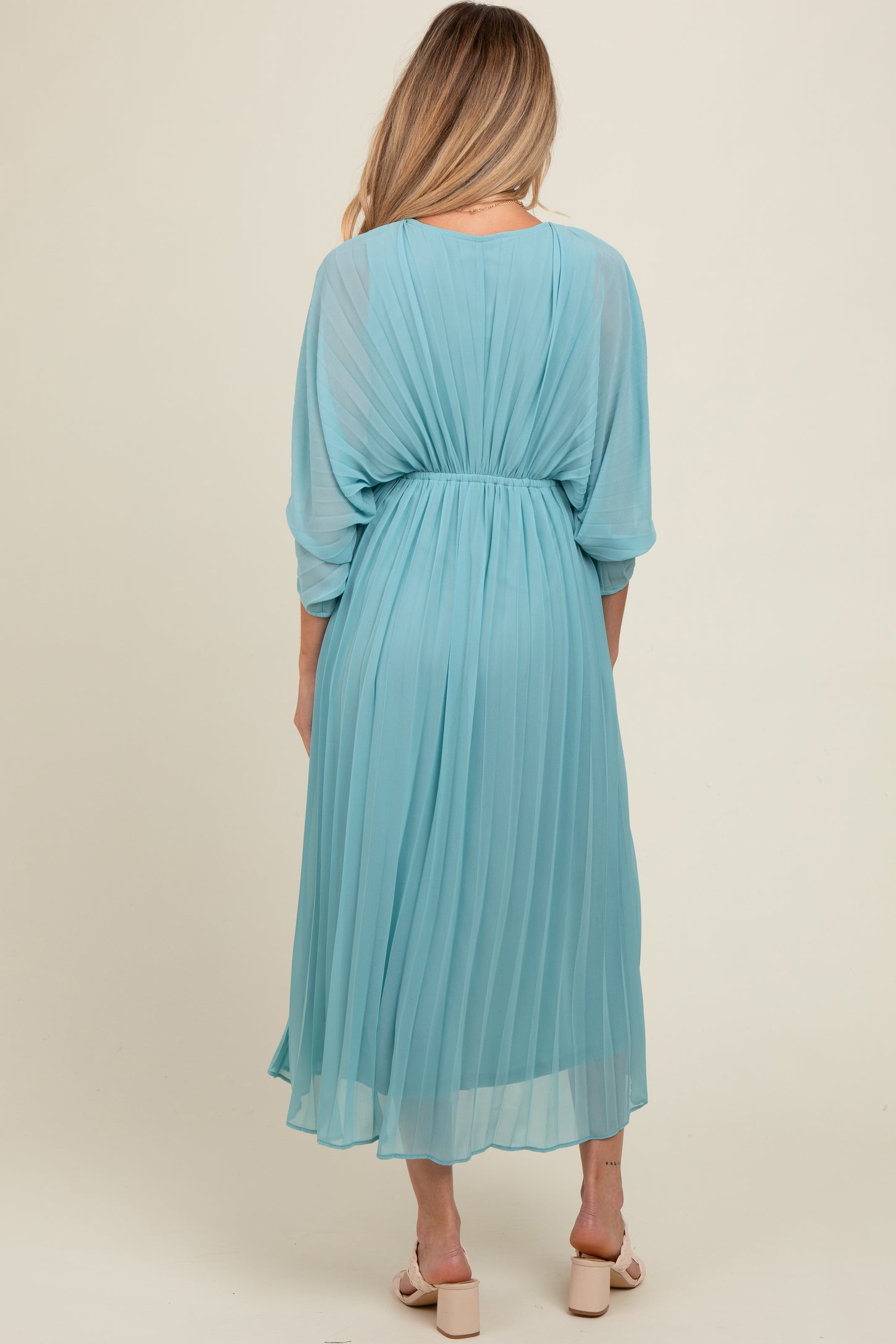 woman wearing a flowy light blue pleated maternity dress with a cinched waist and three-quarter sleeves