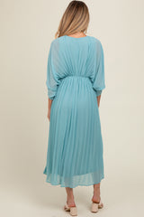 woman wearing a flowy light blue pleated maternity dress with a cinched waist and three-quarter sleeves
