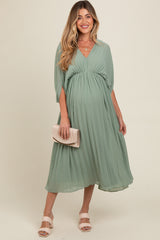 woman wearing a mint green pleated maternity dress with a v-neck and flowing sleeves, holding a clutch and showing a baby bump