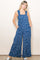woman wearing a blue floral print jumpsuit with wide legs and adjustable straps, standing with pockets in front