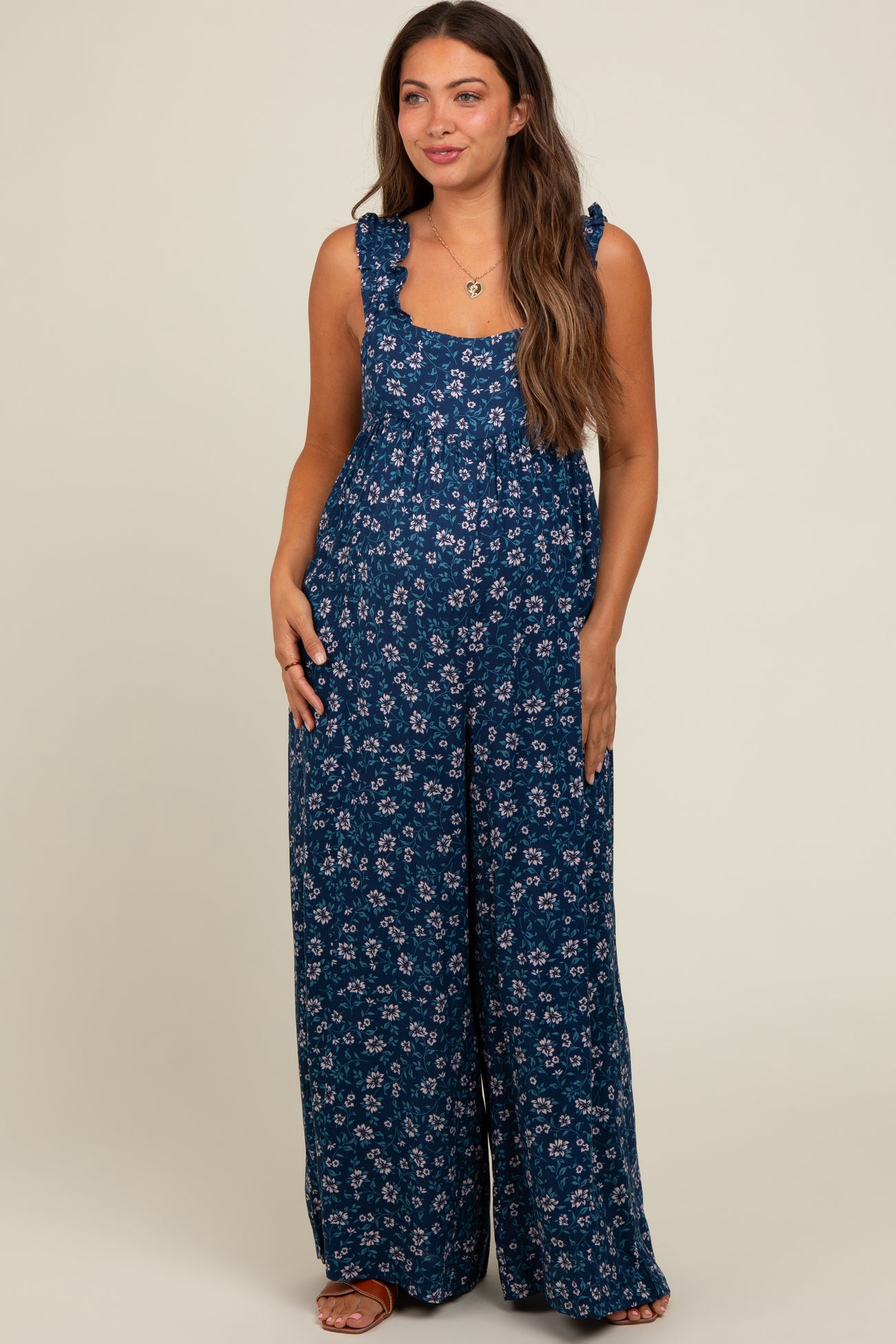 woman wearing a navy blue floral maternity jumpsuit with ruffle straps and wide legs, showing her baby bump