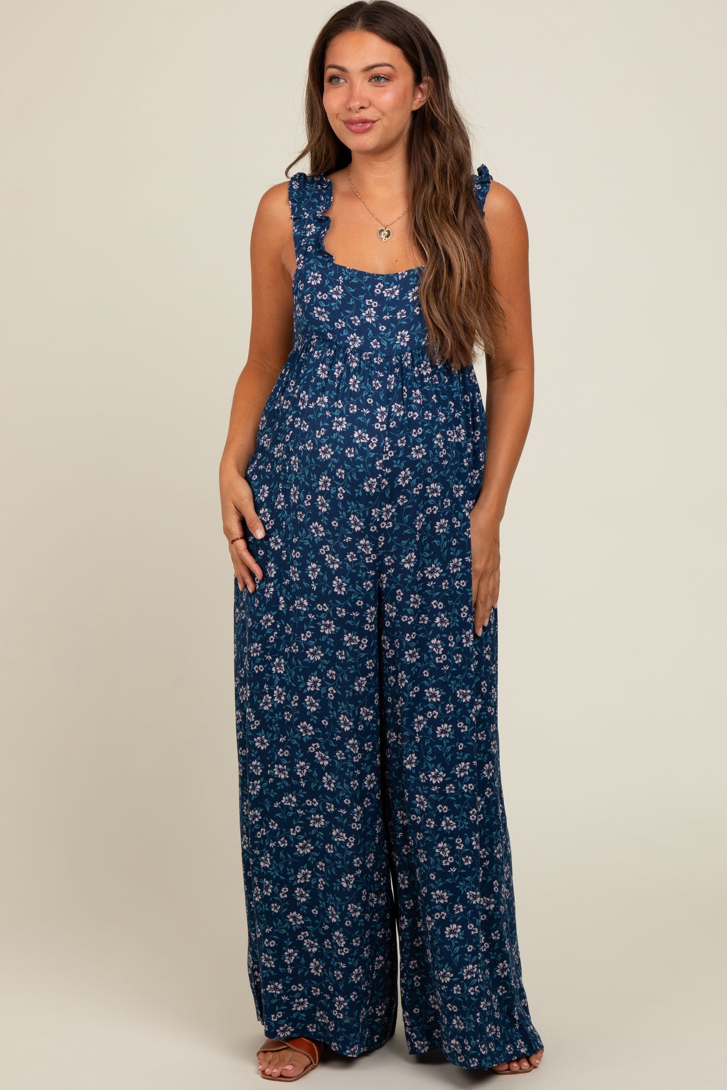 woman wearing a navy blue floral maternity jumpsuit with ruffle straps and wide legs, showing her baby bump