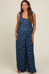 woman wearing a navy blue floral maternity jumpsuit with ruffle straps and wide legs, showing her baby bump