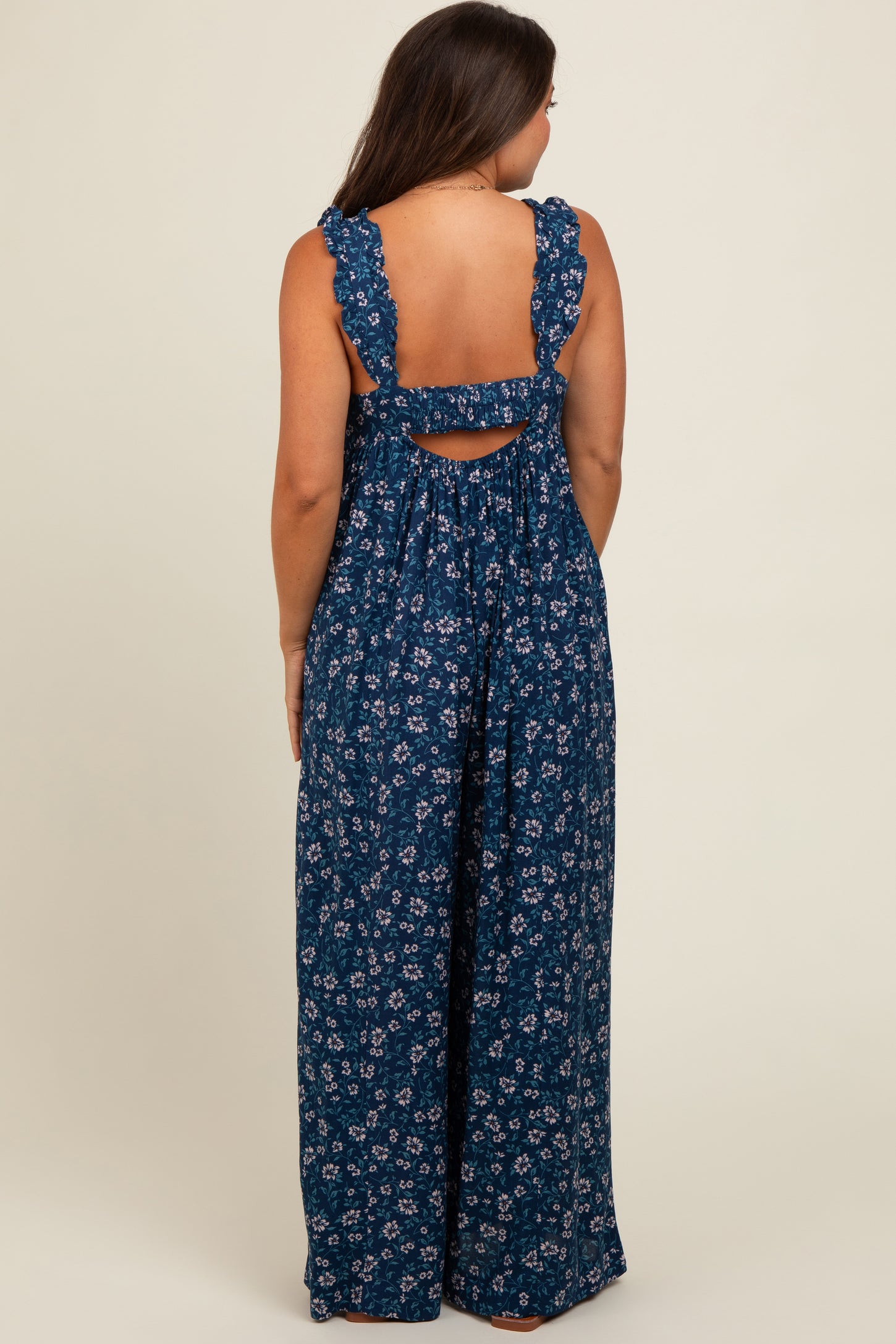 woman wearing a navy blue floral maternity jumpsuit with ruffled straps and a back cutout