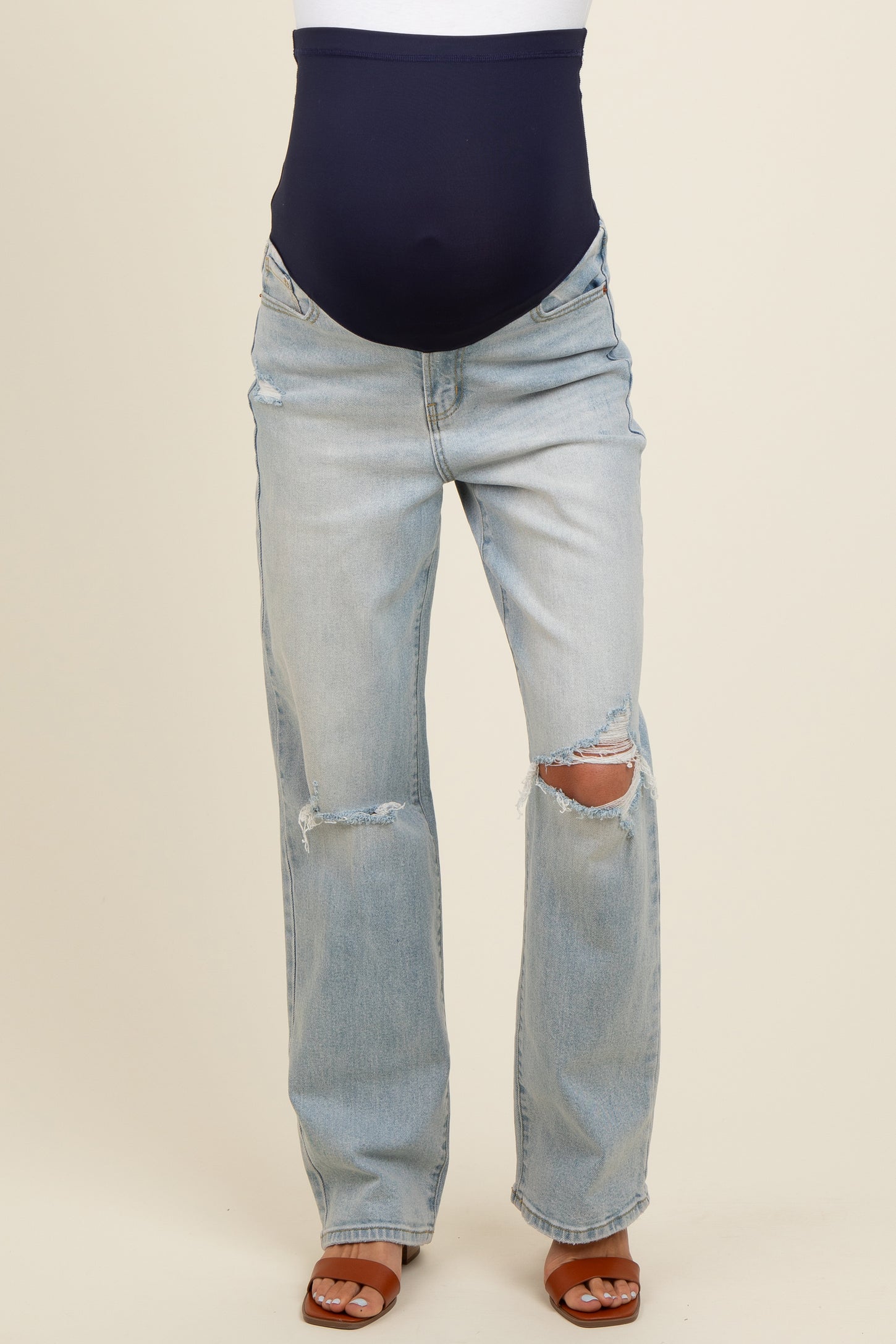 woman wearing light wash distressed maternity jeans with a navy over-the-bump waistband and brown heeled sandals