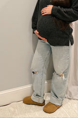 woman wearing a dark gray sweater and distressed light blue maternity jeans, cradling her baby bump
