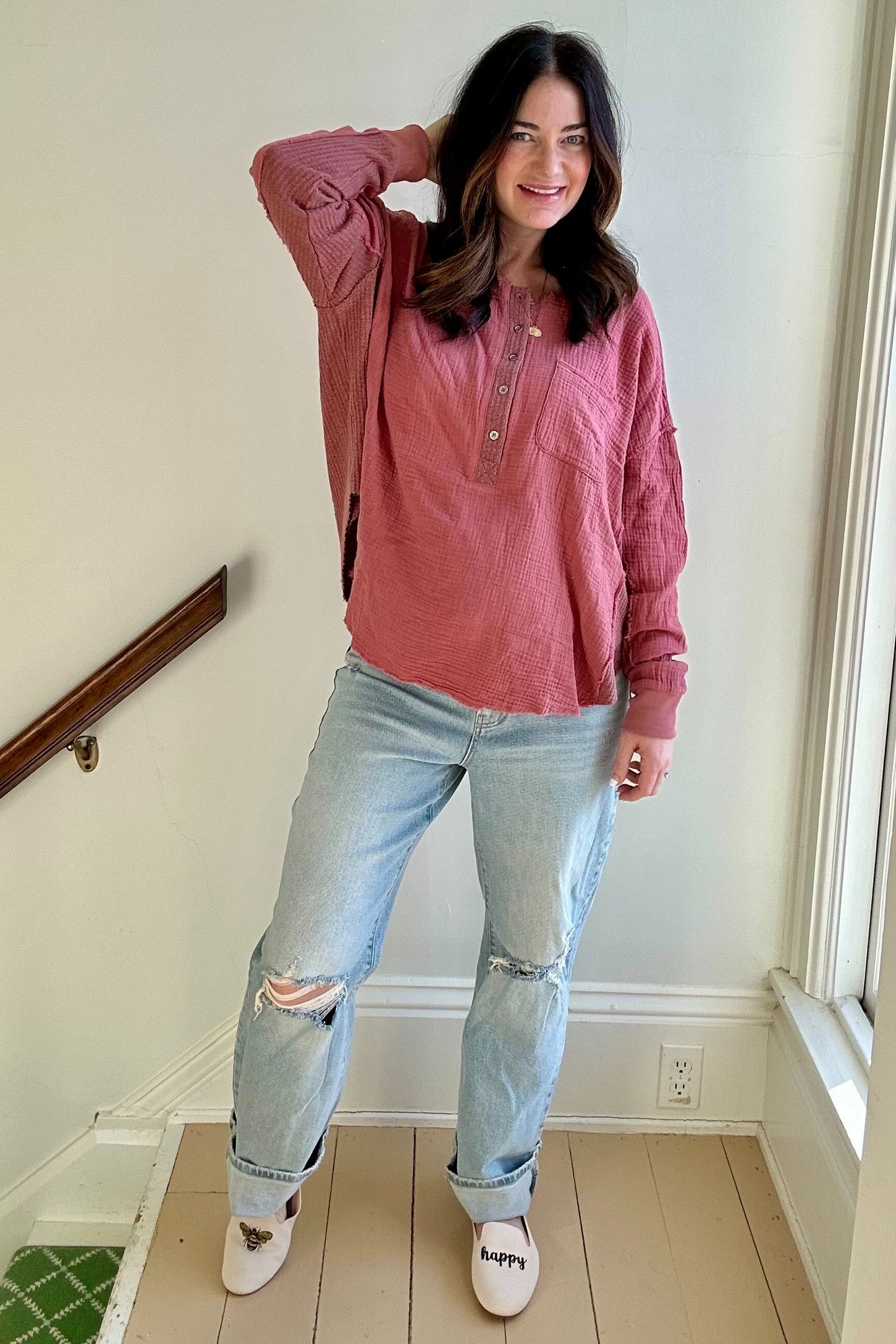 woman wearing a dusty rose maternity top with button details and distressed light wash jeans, standing with one hand on her hip