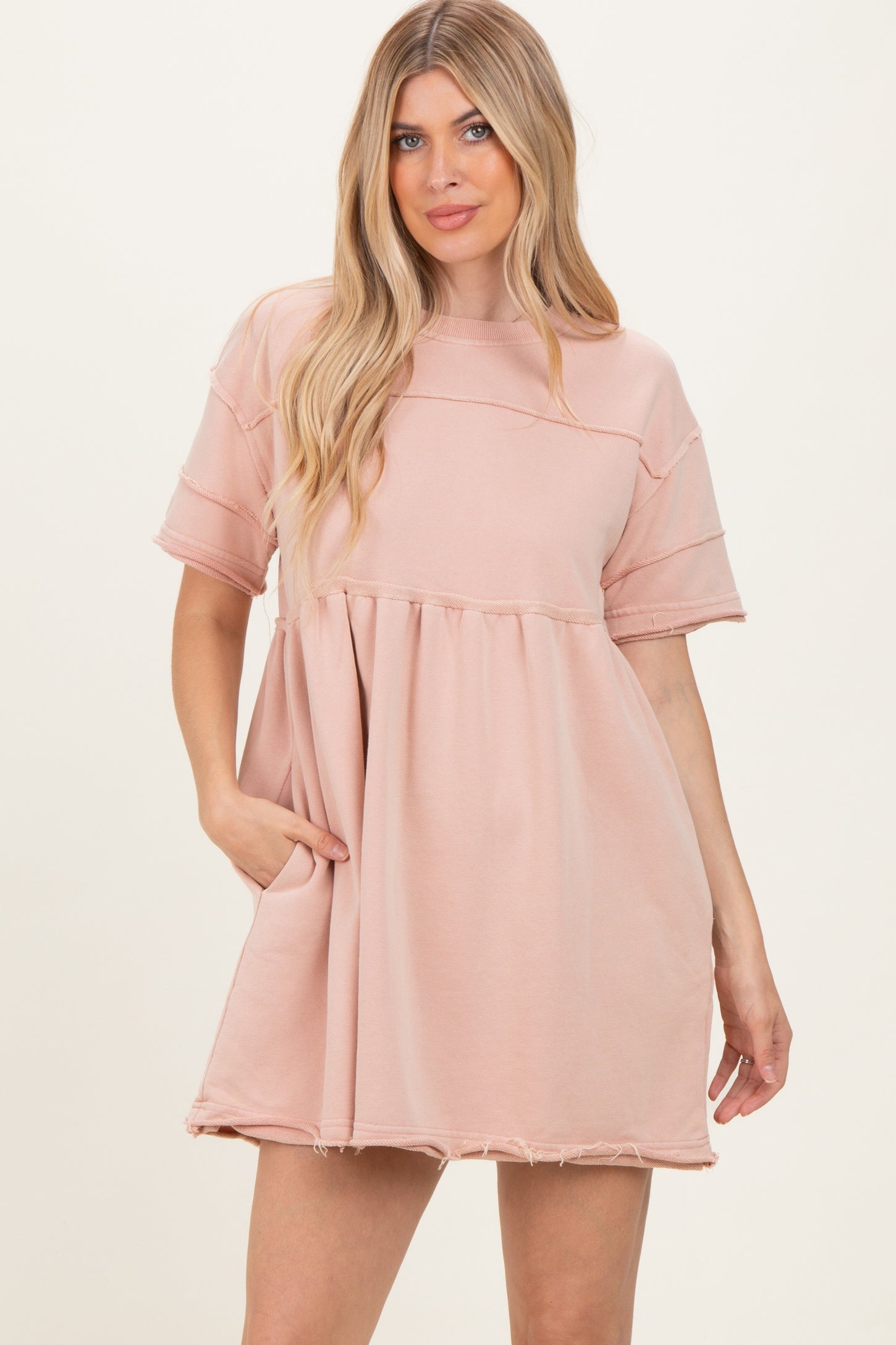 woman wearing a blush pink oversized short sleeve dress with a tiered design and side pockets