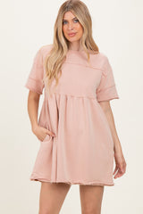 woman wearing a blush pink oversized short sleeve dress with a tiered design and side pockets