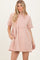 woman wearing a blush pink oversized short sleeve dress with a tiered design and side pockets