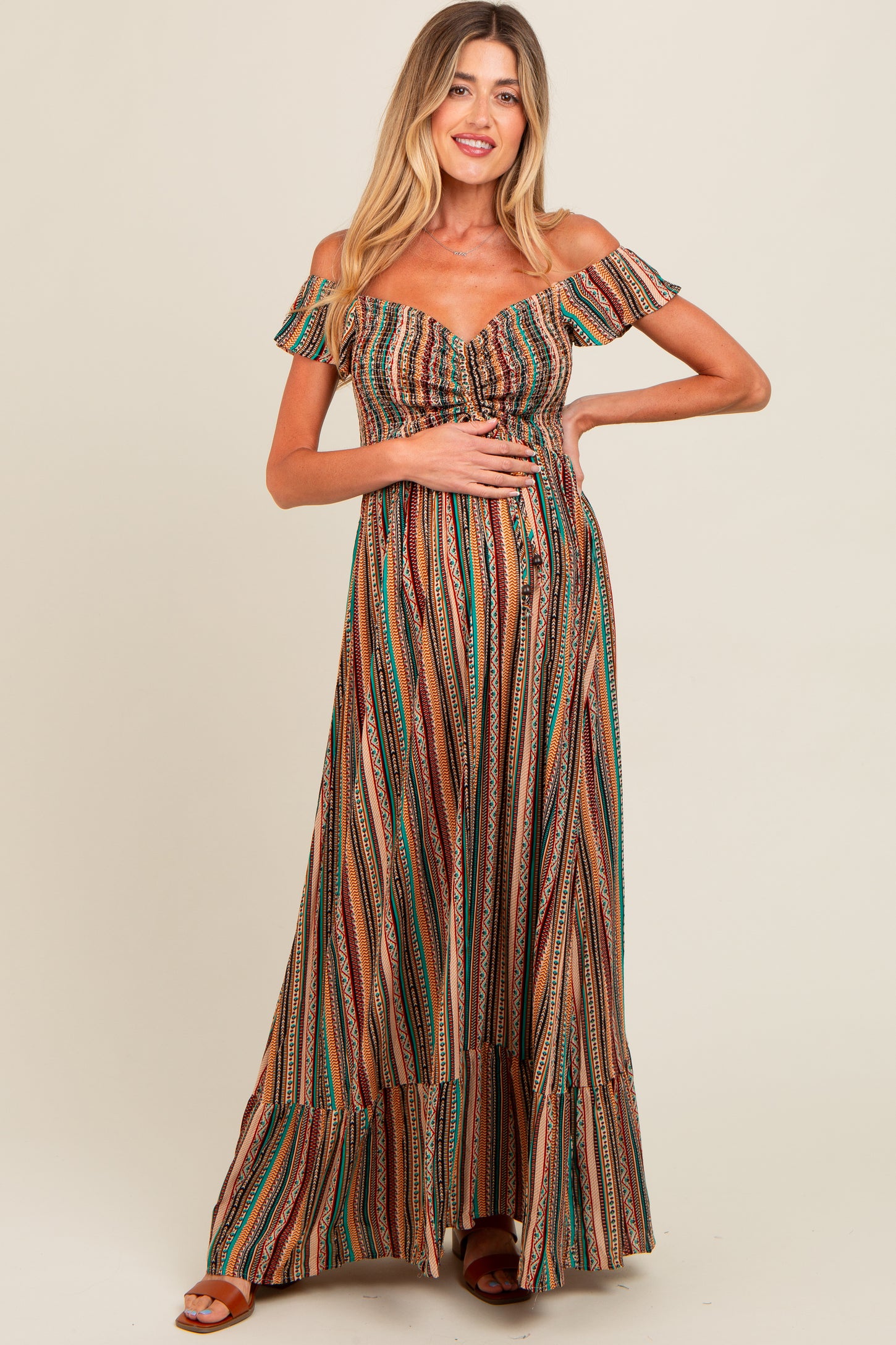 woman wearing a multi-colored striped off-the-shoulder maternity dress and showing her baby bump