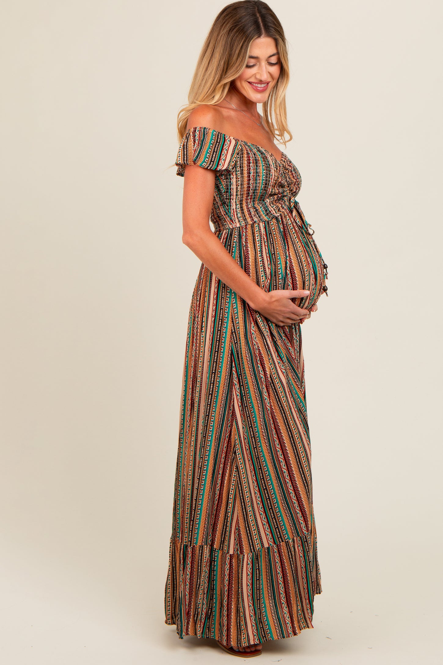 woman wearing a striped off-shoulder maternity maxi dress and holding her baby bump