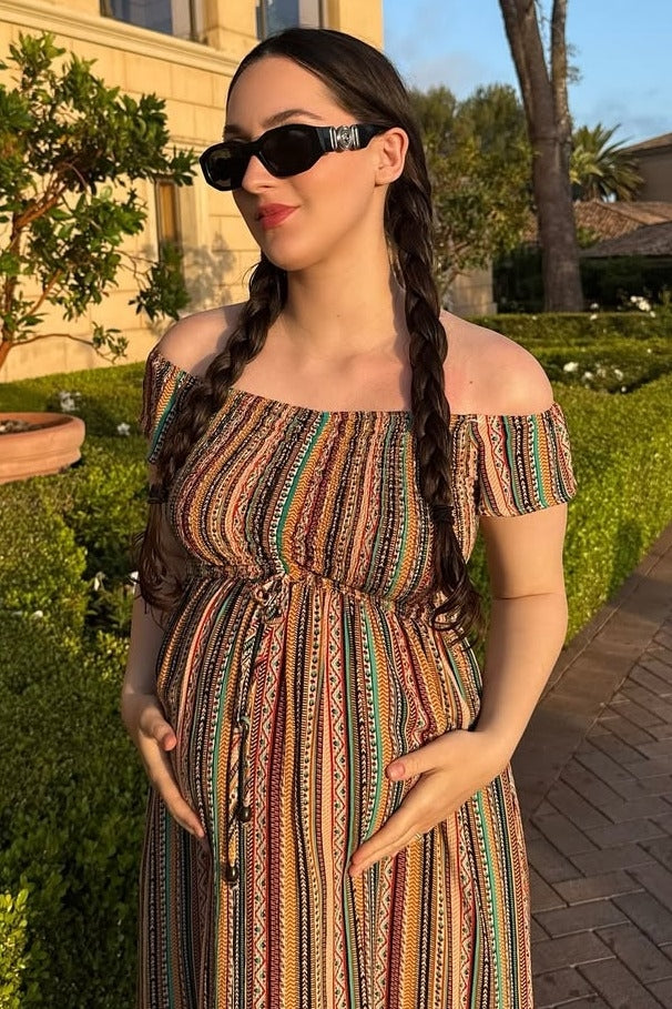 woman wearing a multicolored off-the-shoulder maternity dress and holding her baby bump