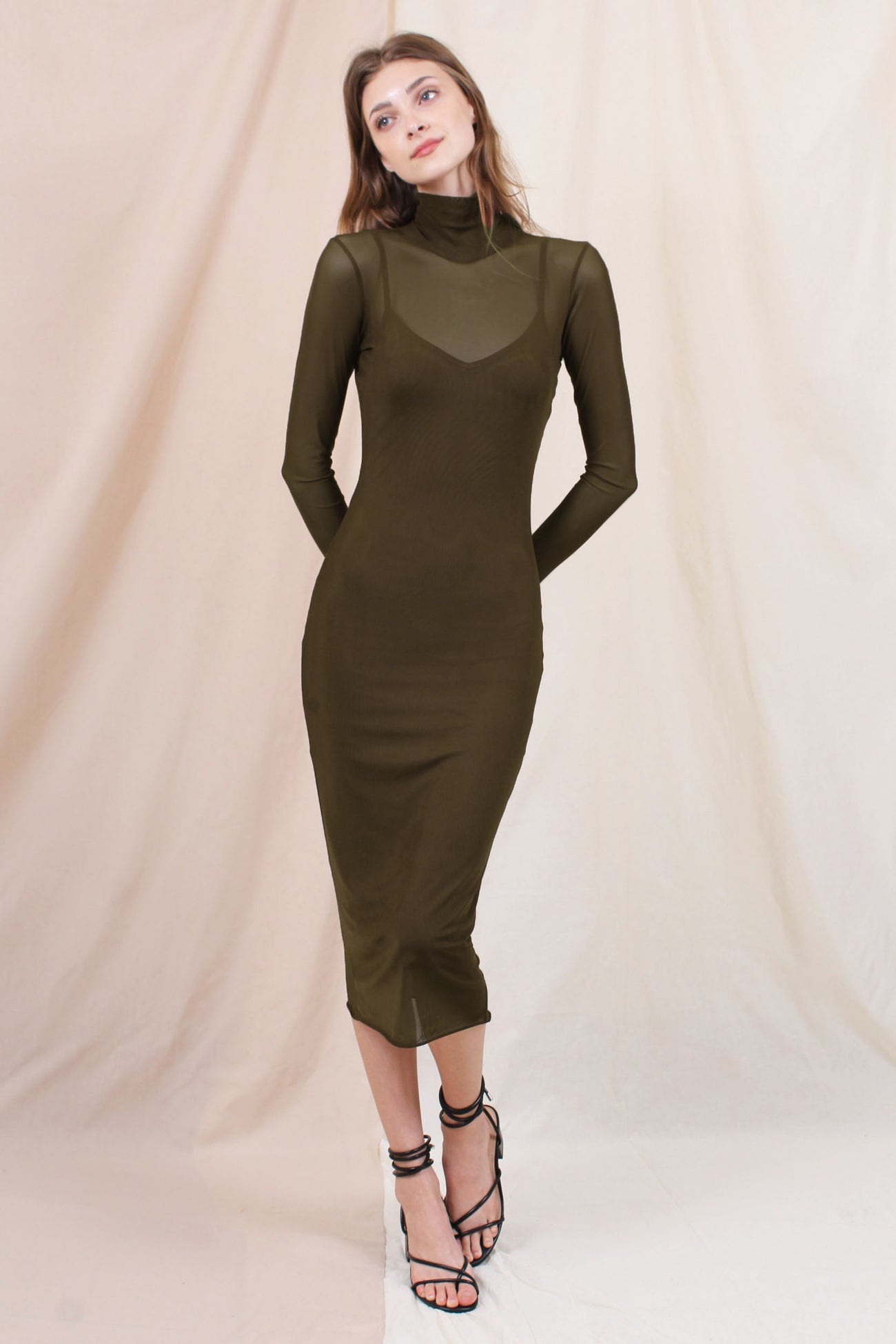 woman wearing an olive green long sleeve fitted dress with a sheer neckline and strappy heels