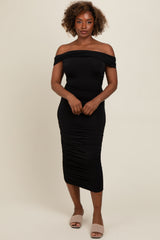 woman wearing a black off-shoulder bodycon midi dress with ruching details and slip-on beige sandals