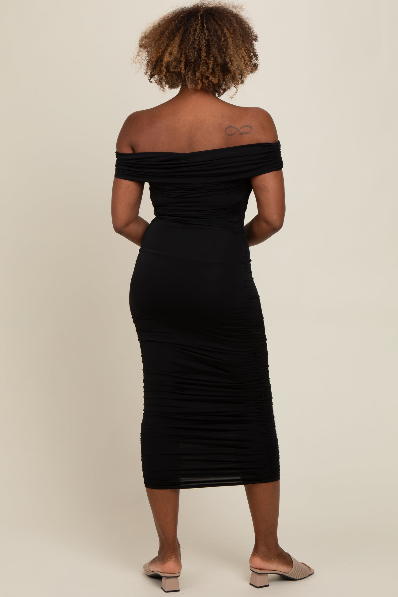 woman wearing a black off-shoulder ruched midi dress viewed from the back