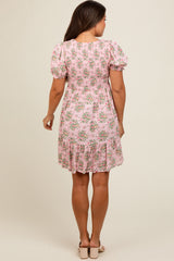 woman wearing a floral pink maternity dress with puff sleeves and a tiered hem, showcasing her baby bump from behind