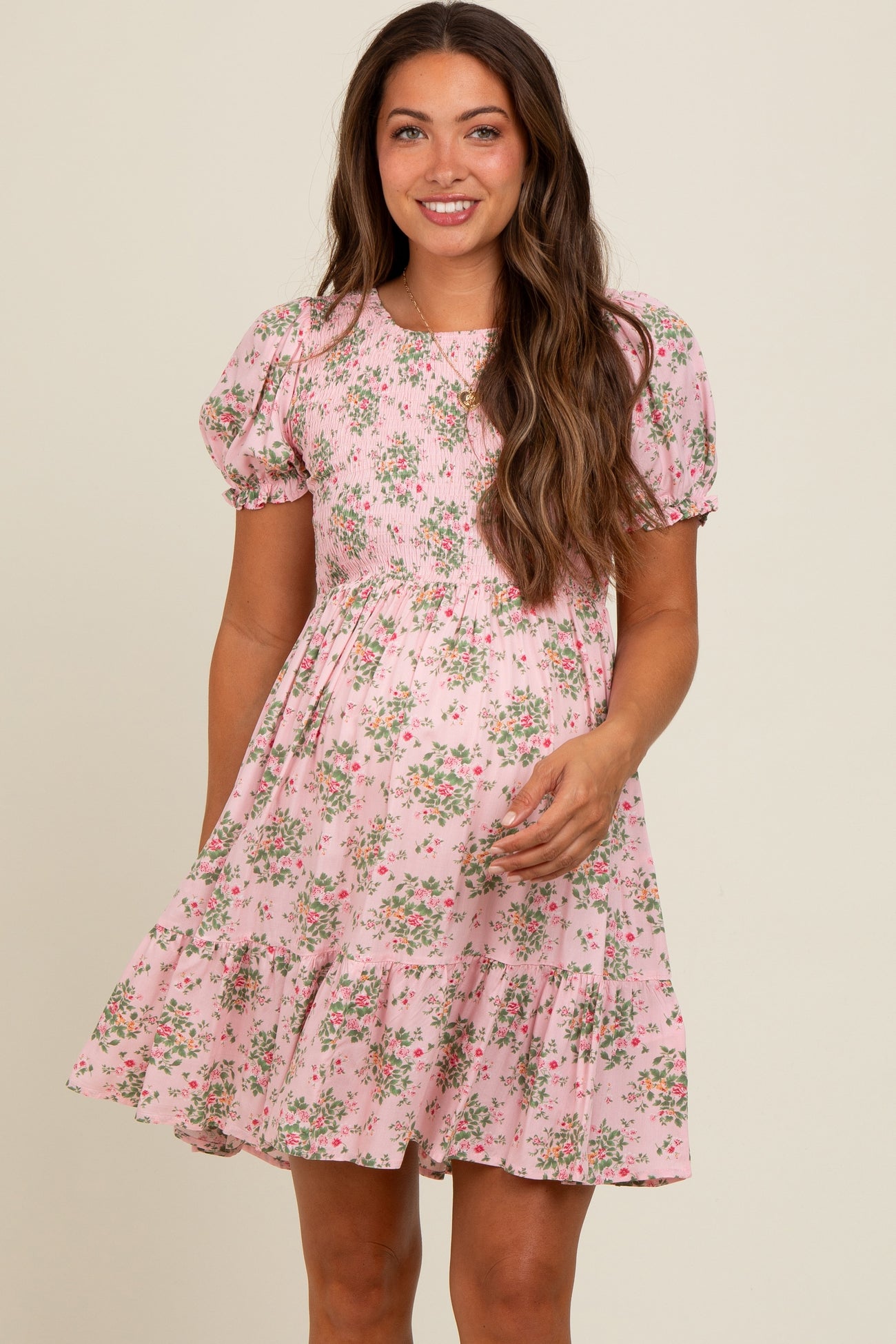 woman wearing a short puff sleeve pink floral maternity dress with a tiered skirt and smiling at the camera