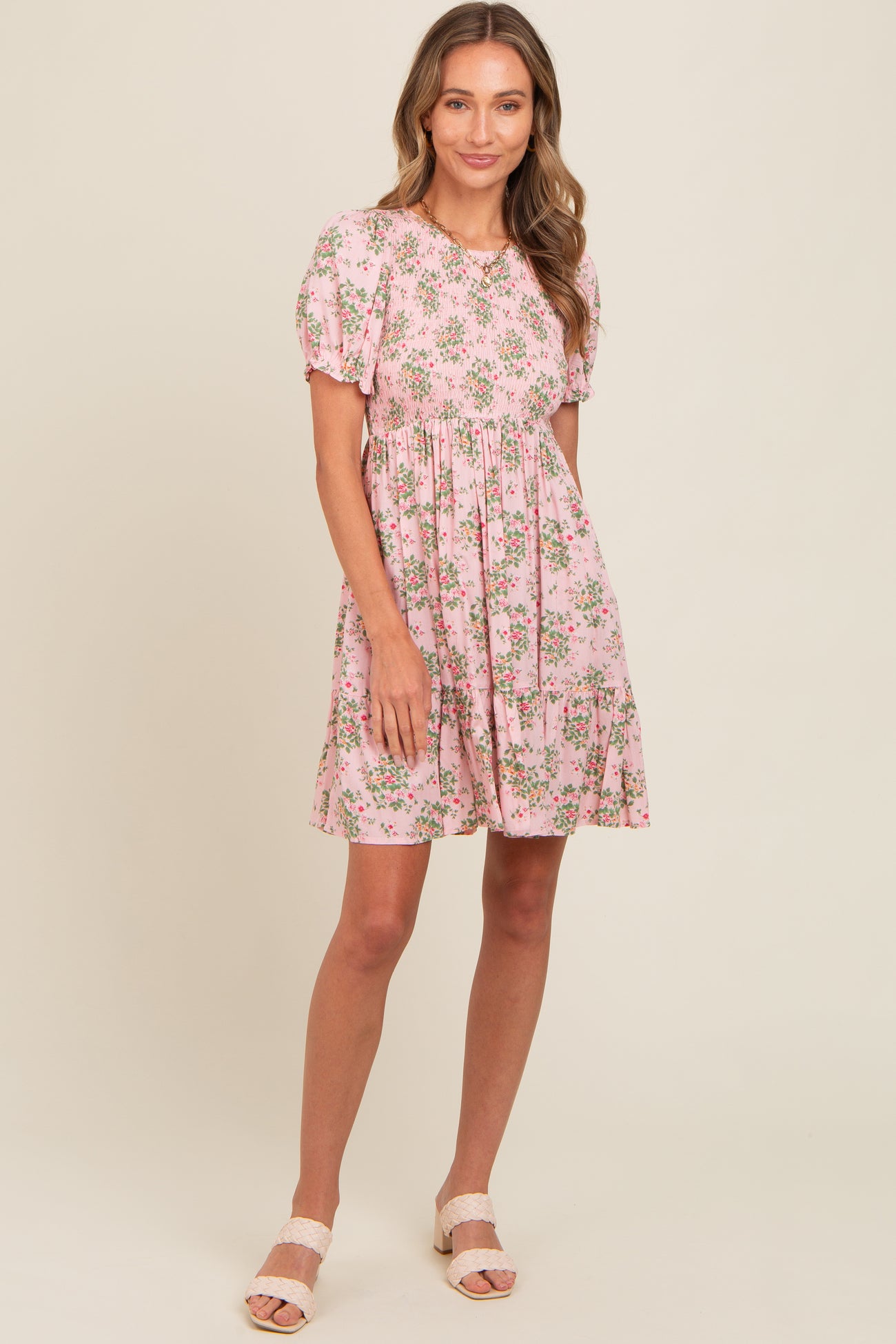 woman wearing a short pink floral dress with puff sleeves and a tiered skirt, standing and smiling