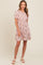 woman wearing a short pink floral dress with puff sleeves and a tiered skirt, standing and smiling