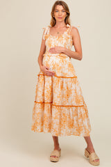 woman wearing a floral maternity dress in orange and white, holding her baby bump with a relaxed fit and tiered design