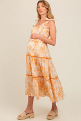 woman wearing a flowy orange floral maternity dress with ruffle straps and a visible baby bump