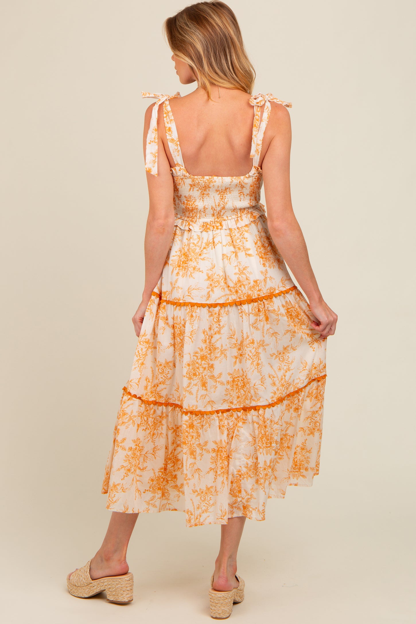 woman wearing a white and orange floral maternity dress with tie shoulder straps and a tiered skirt, showing a baby bump