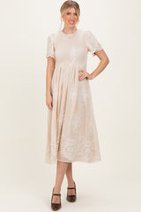 woman wearing a beige short sleeve midi dress with lace details and a fitted bodice, standing and smiling