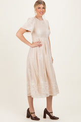 woman wearing a beige midi dress with floral embroidery and short sleeves, standing with one hand on her hip