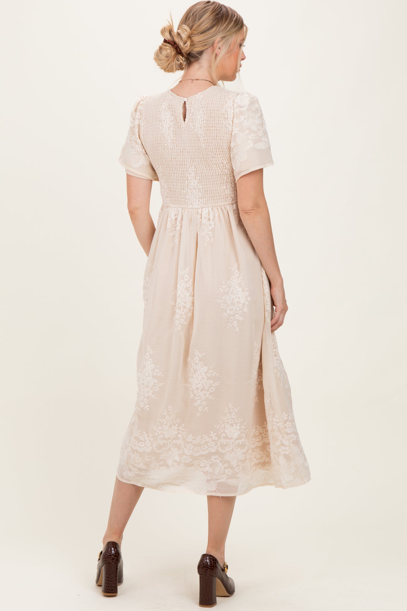 woman wearing a back view of a light beige midi dress with floral embroidery and short sleeves
