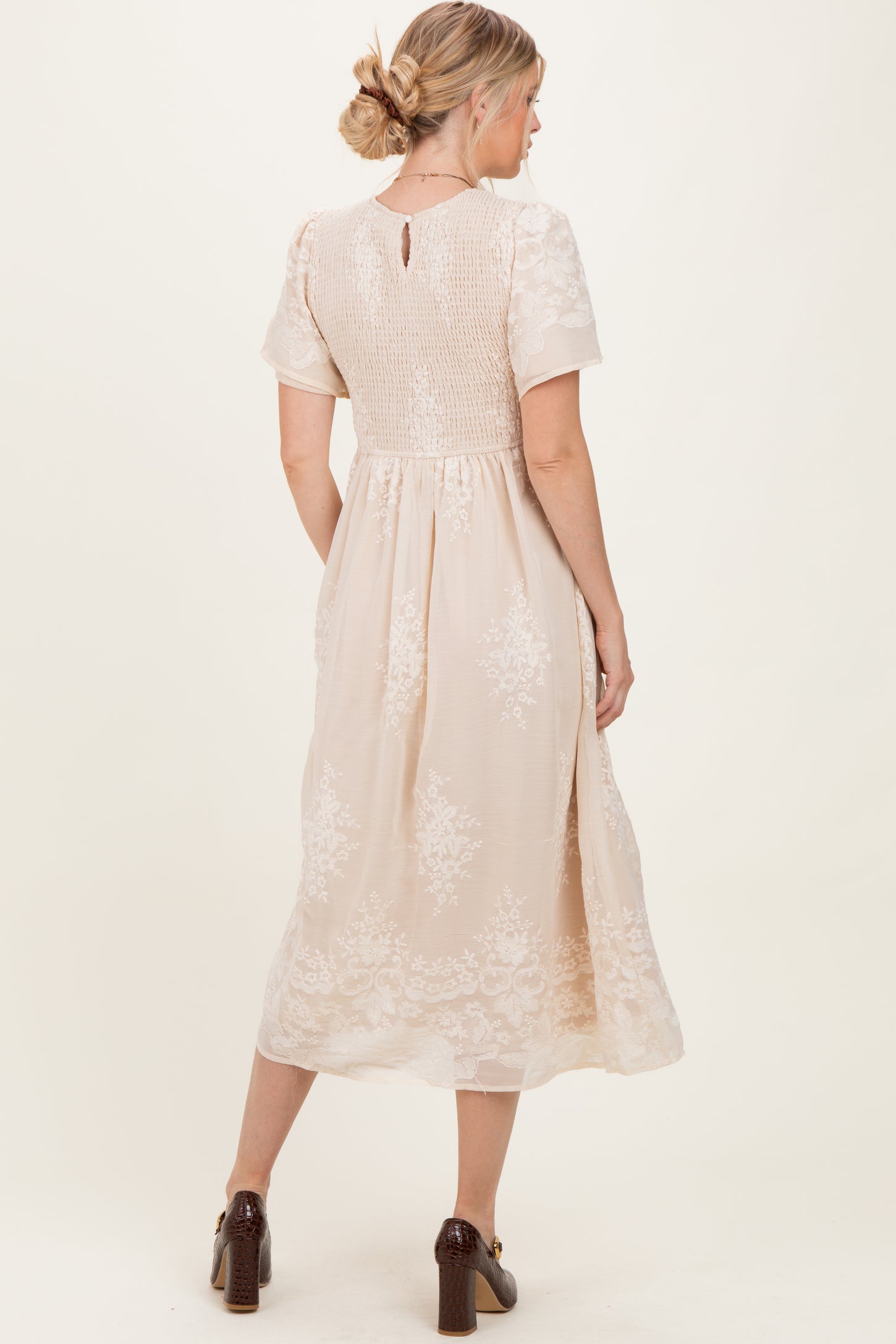 woman wearing a back view of a light beige midi dress with floral embroidery and short sleeves